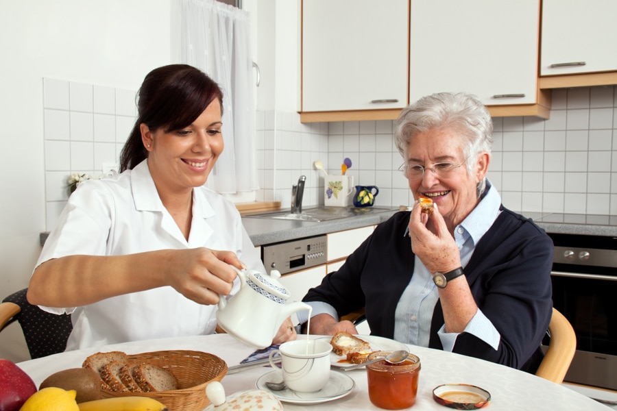a geriatric nurse helps elderly woman at breakfast. elder care of seniors